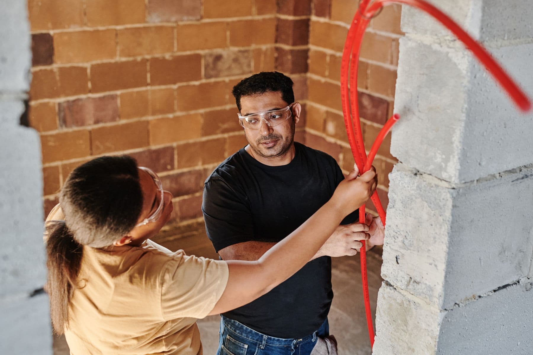 Two tradespeople running new pipe together on a job — the trade passed down a generation