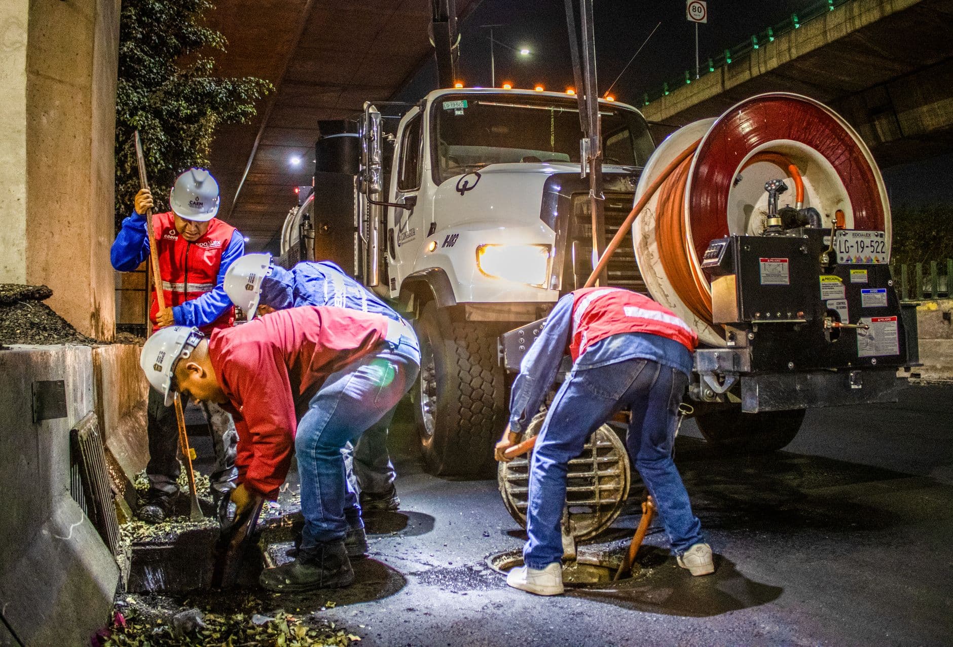 A drain crew clearing a main sewer line at night with a jetting truck