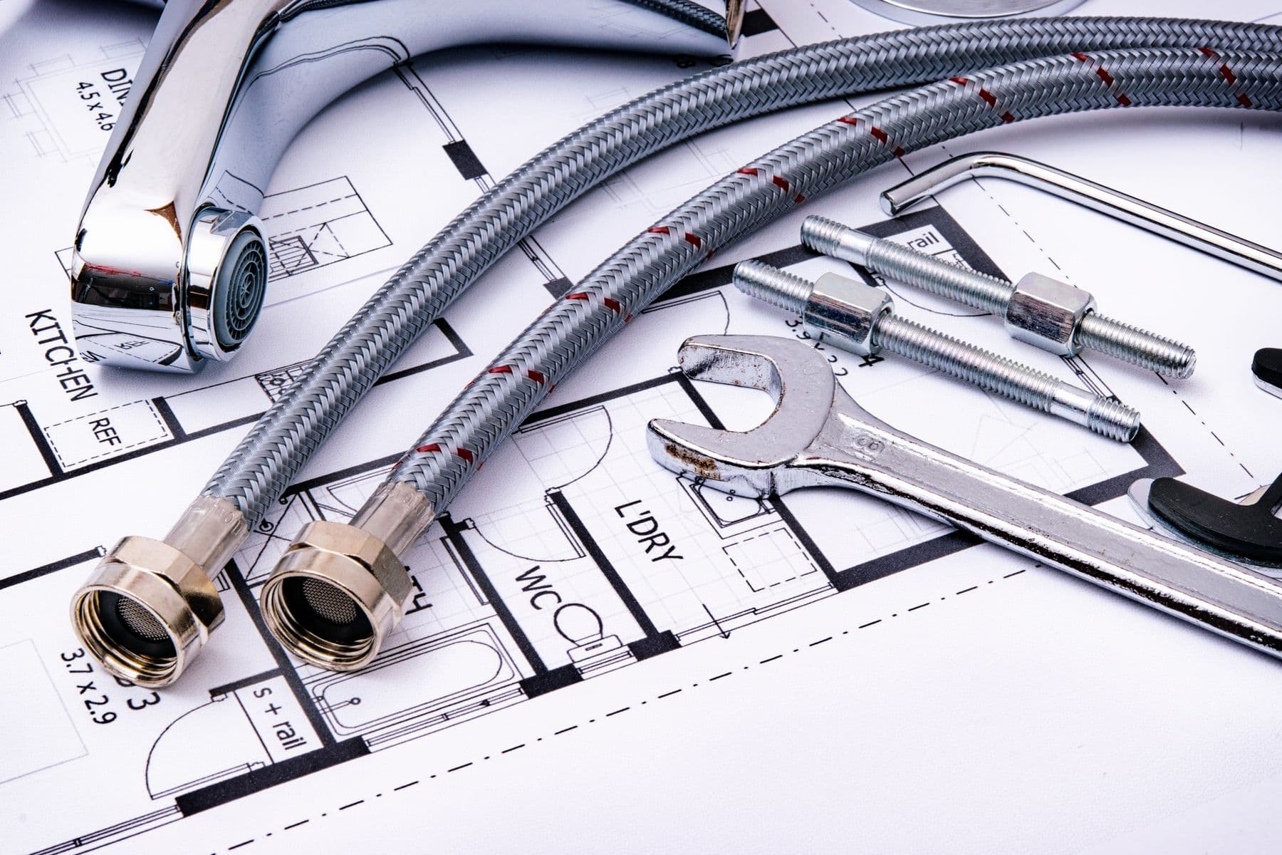 Plumbing tools, braided supply lines, and a pipe wrench arranged on a kitchen plan
